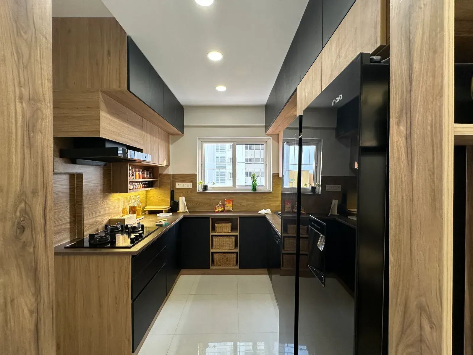 Black and oak parallel kitchen seen through a glass door — The Aakar